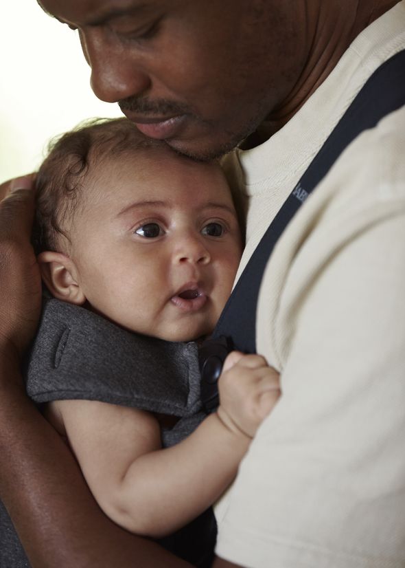 A man gently holds a baby in a carrier, both looking content and peaceful.