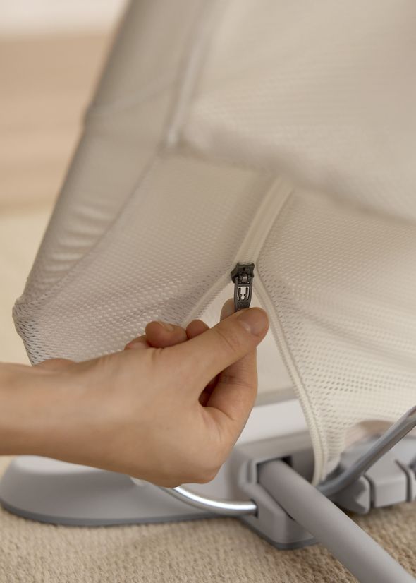 A hand unzipping a white mesh fabric cover from a piece of furniture on a carpeted floor.
