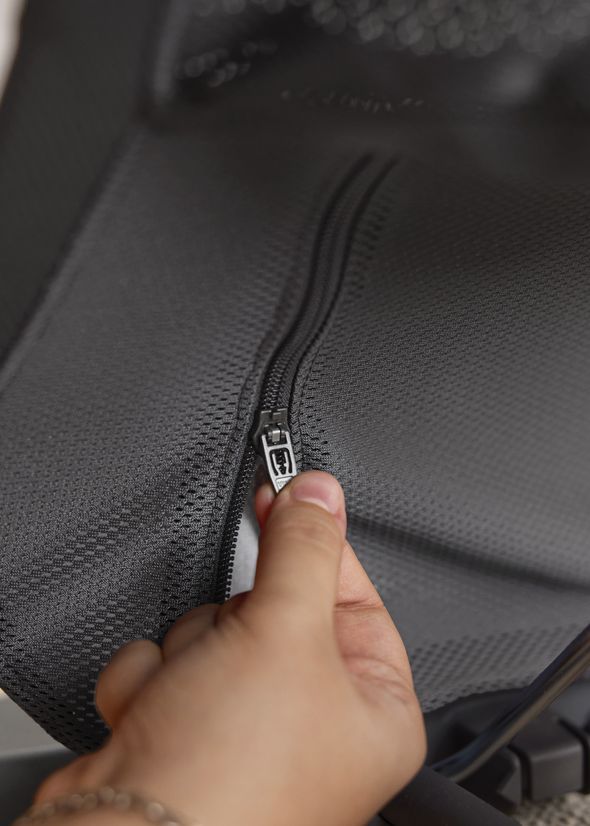A close-up of a hand gripping a zipper on textured black fabric.