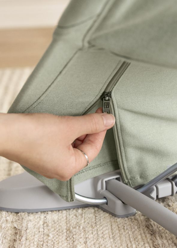 Hand zipping up a light green fabric cover on a metal frame, over a textured beige rug.