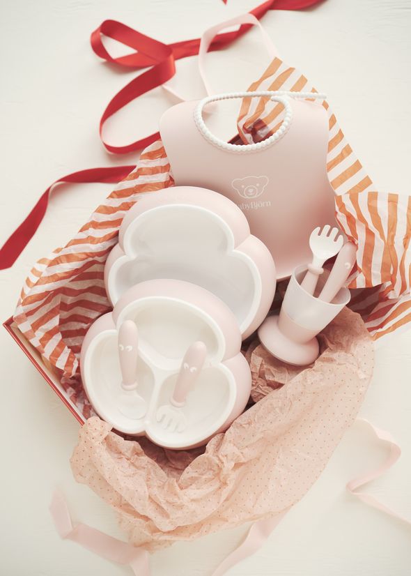 Pink and white baby feeding set with plates, utensils, and a bib in a gift box lined with striped and polka dot tissue paper.