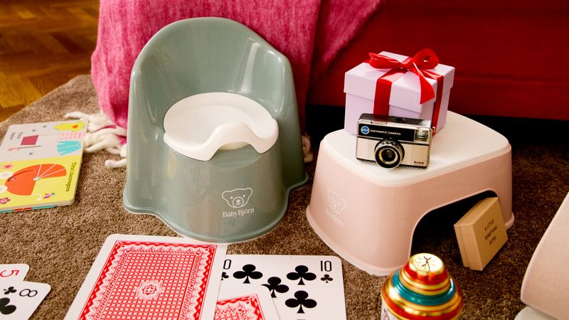 Children's potty and step stool with a camera, gift box, playing cards, and toys on a carpeted floor.