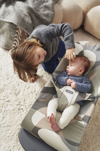 Baby in a BabyBjörn bouncer with bigger sister playing with him