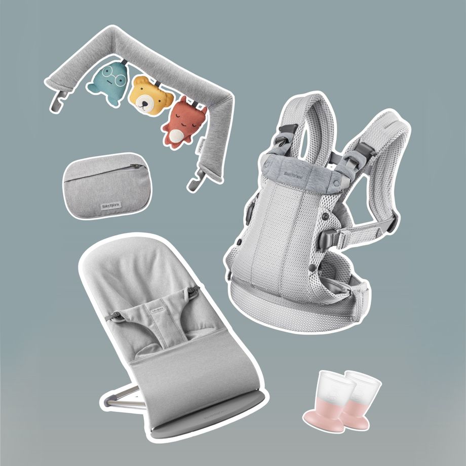 Baby products on a light grey background: carrier, bouncer, toy arch with animals, diaper bag, and two pink baby bottles.