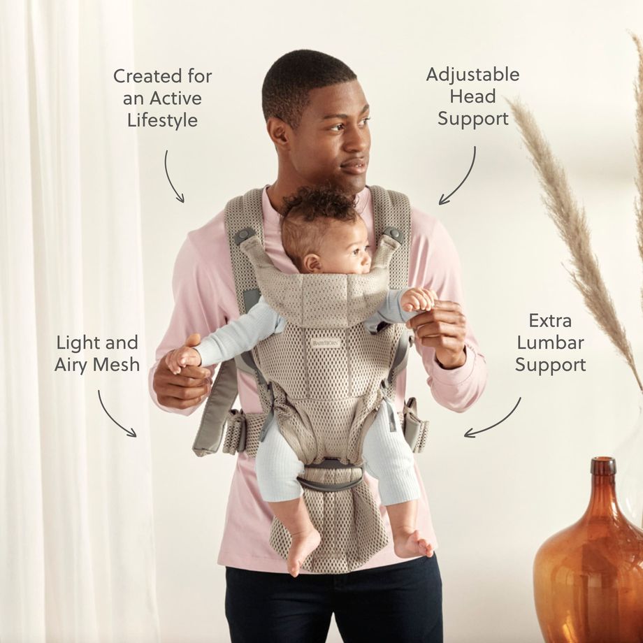 Man wearing gray mesh baby carrier with infant facing forward; labels show adjustable head, extra lumbar support and breathable design.