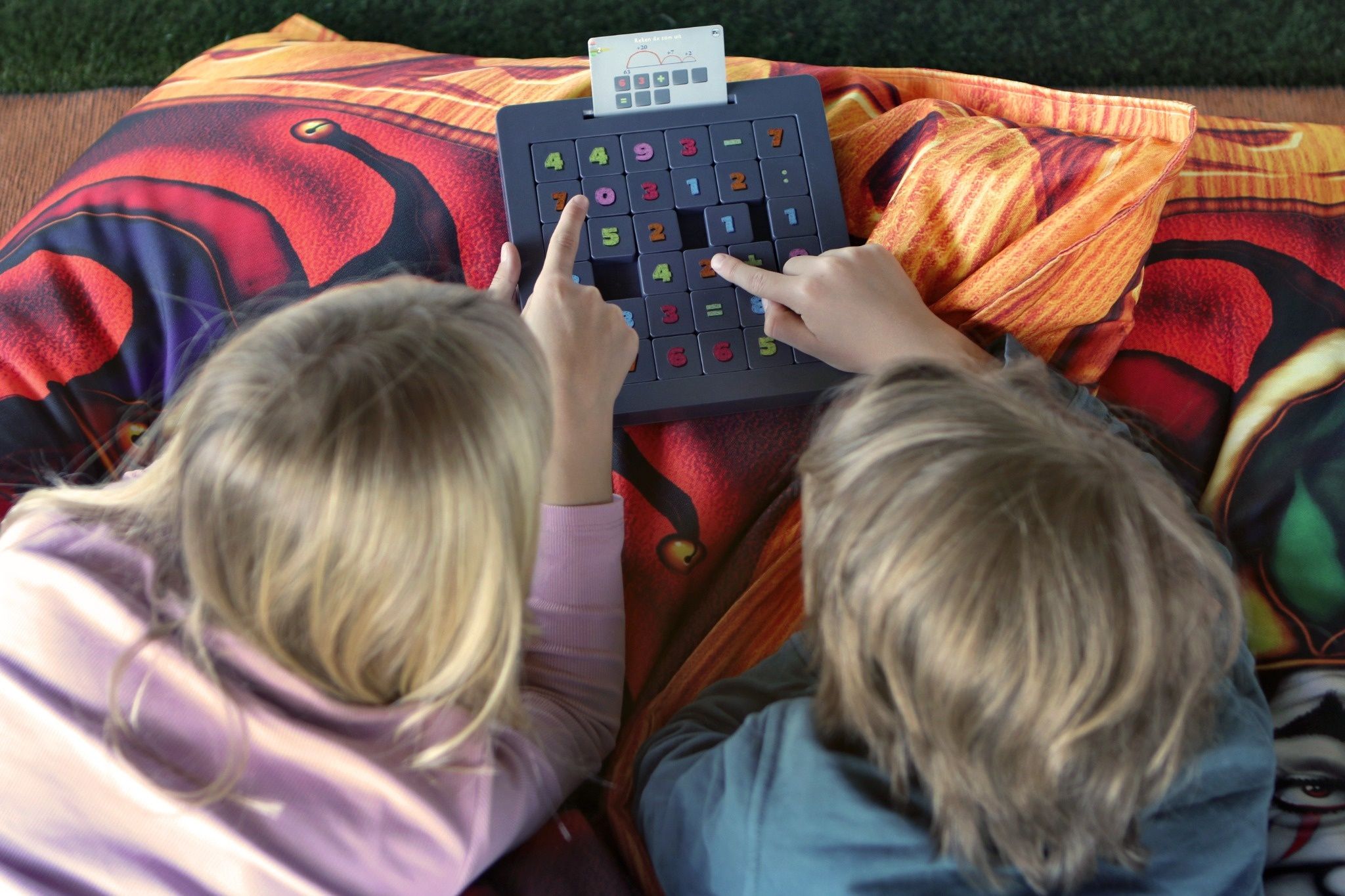 Twee kinderen spelen Schuifpret op een kleurrijk kussen en concentreren zich op het op volgorde leggen van de schuifjes.