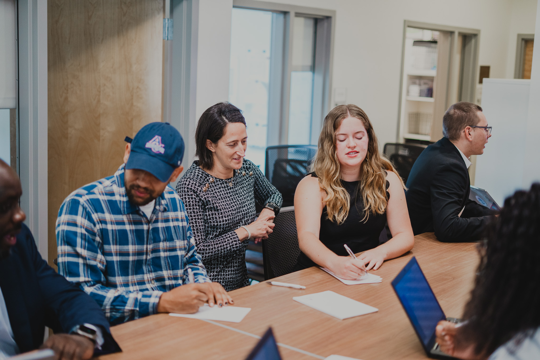 A group of people sitting around a conference table, discussing and taking notes.