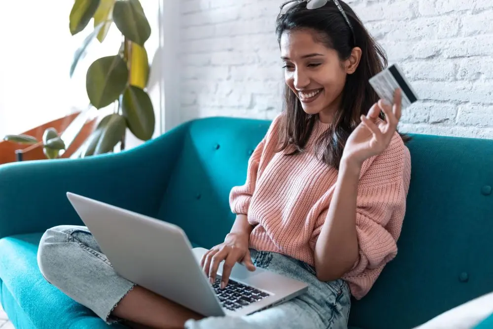 Frau mit Kreditkarte in der Hand blickt auf einen Laptop.