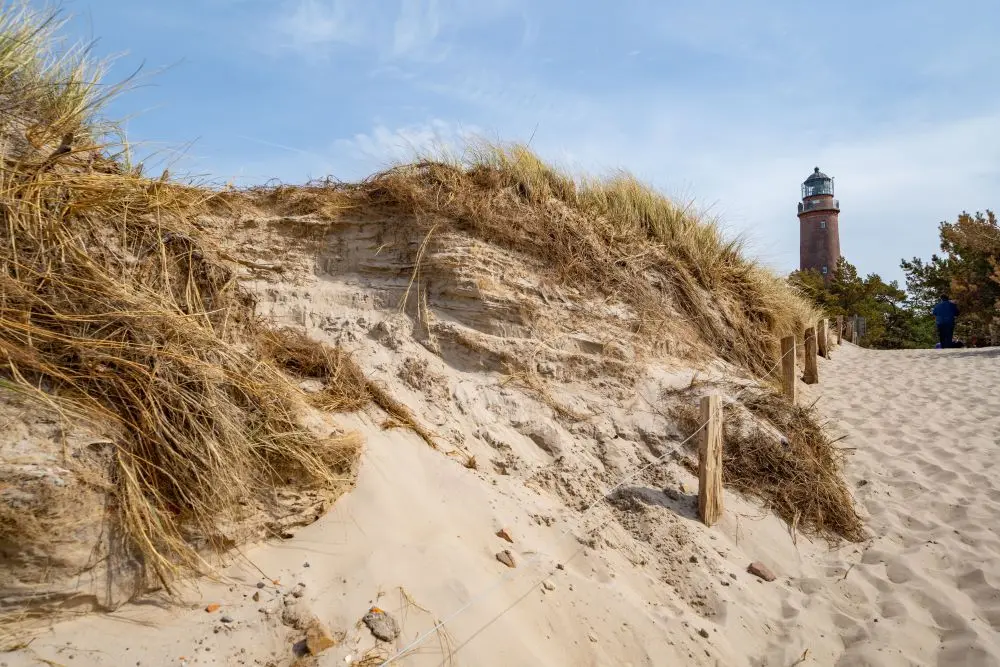Sanddüne am Strand, im Hintergrund ein Leuchtturm.