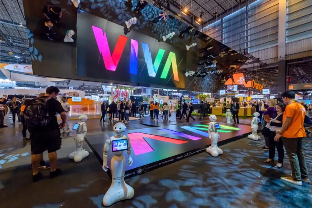 exhibition hall of a technology trade fair with visitors in the foreground a large illuminated sign