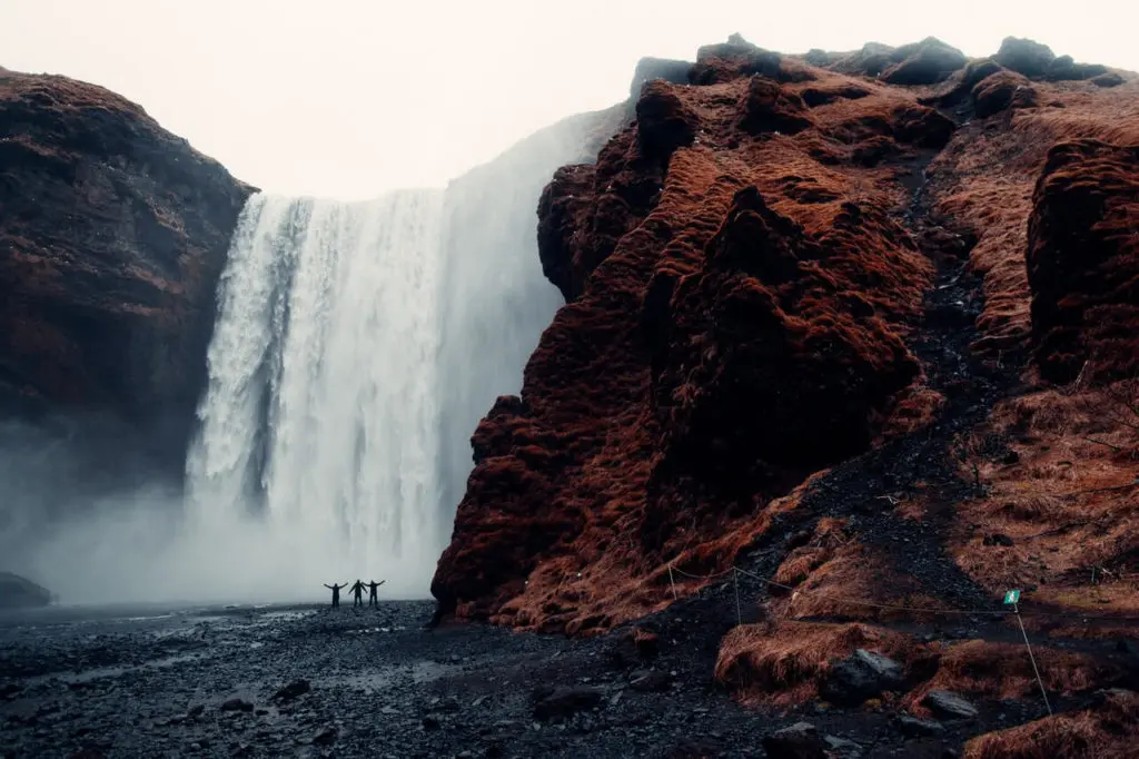 Gruppe steht vor einem Großen Wasserfall umgeben von dunklem Vulkangestein.
