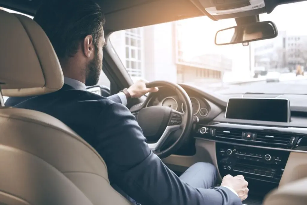 Mann im Anzug sitzt hinter dem Steuer eines Autos.
