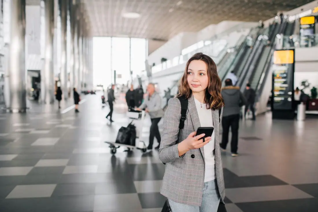 Geschäftsreisende mit Smartphone schaut sich am Flughafen um.