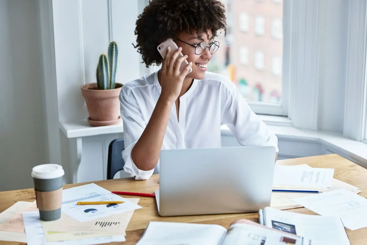 Woman Sitting At Desk Full Of Documents Talking On Phone