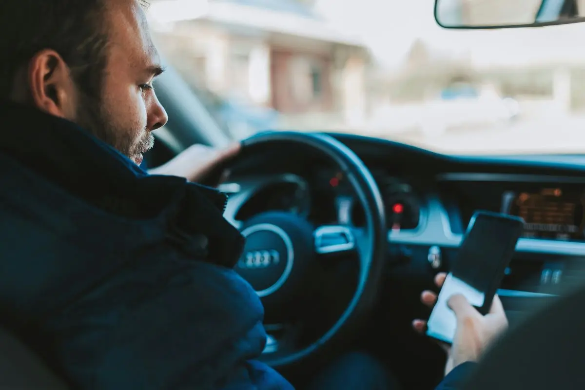 Man Sitting In Car Looking At Mobile Phone