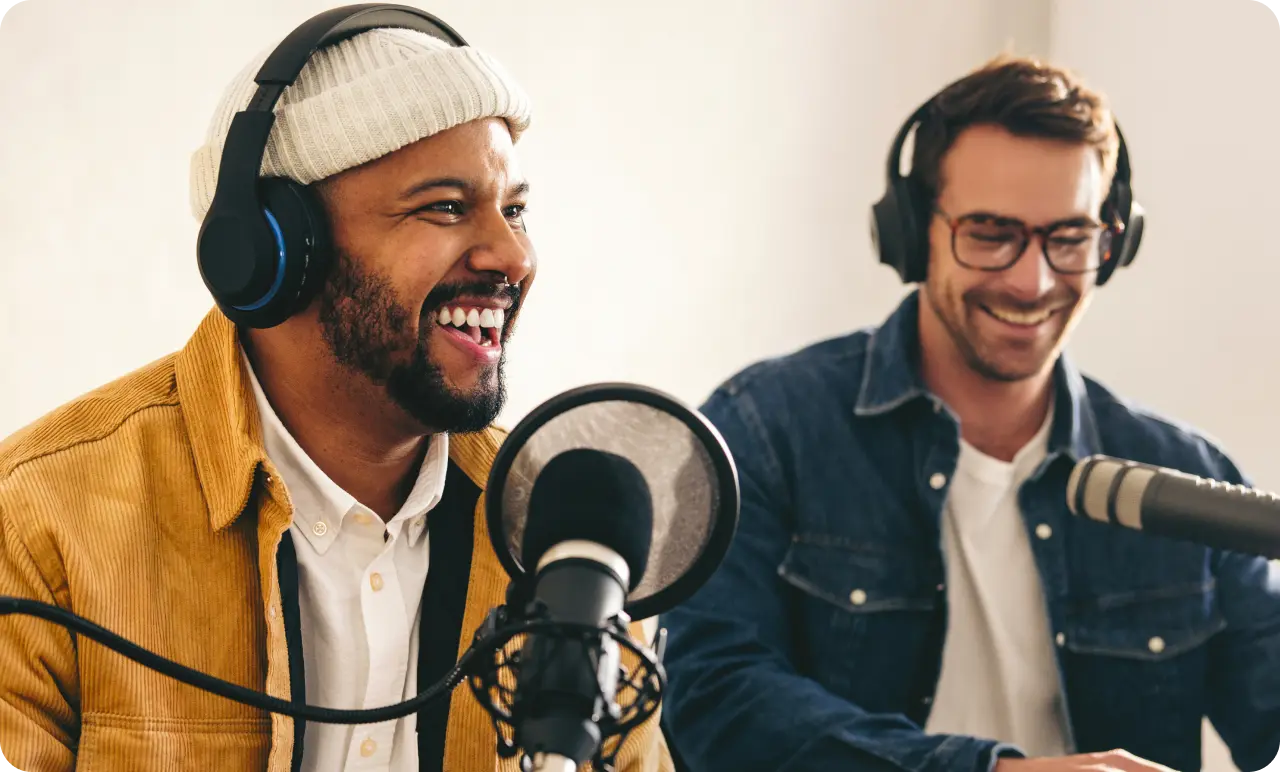 Two men in a studio, wearing headphones and talking into separate microphones.
