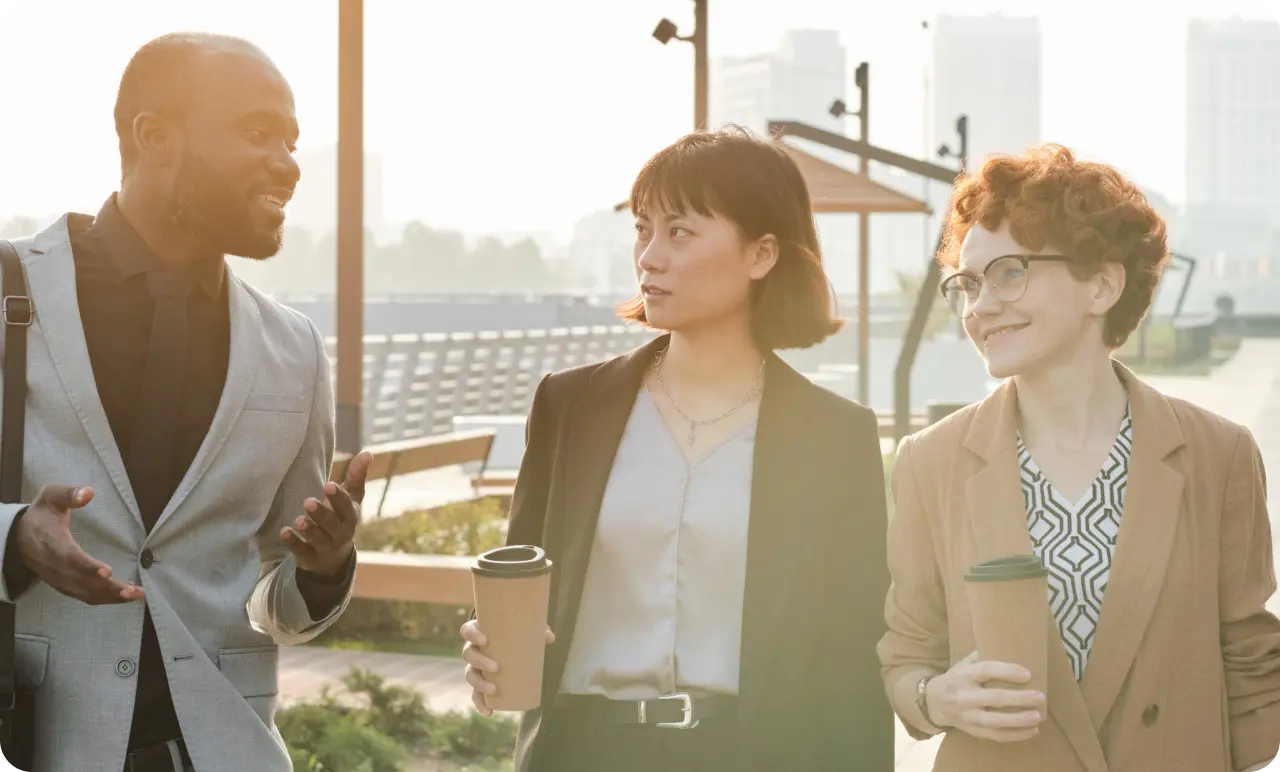 Three colleagues walking together outside drinking coffee.