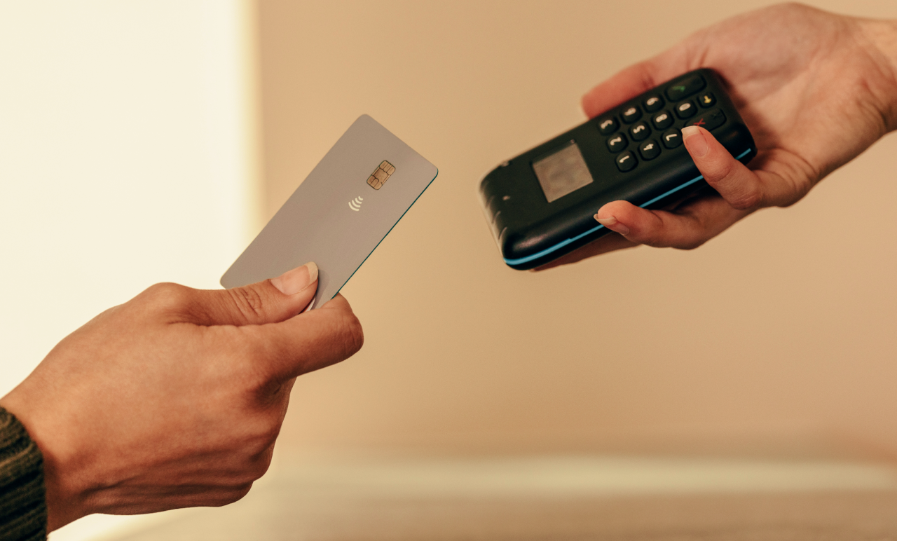 Two hands exchanging a contactless payment: one holds a card, the other a card reader.