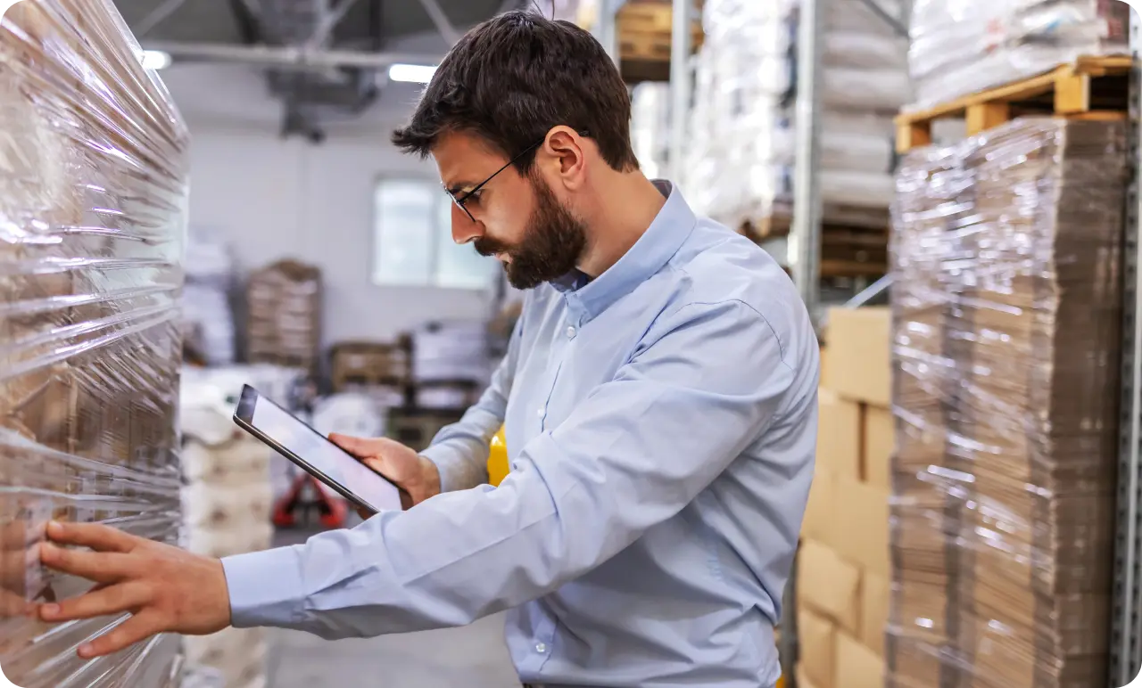 A man taking stock of a delivery on a tablet in a warehouse.