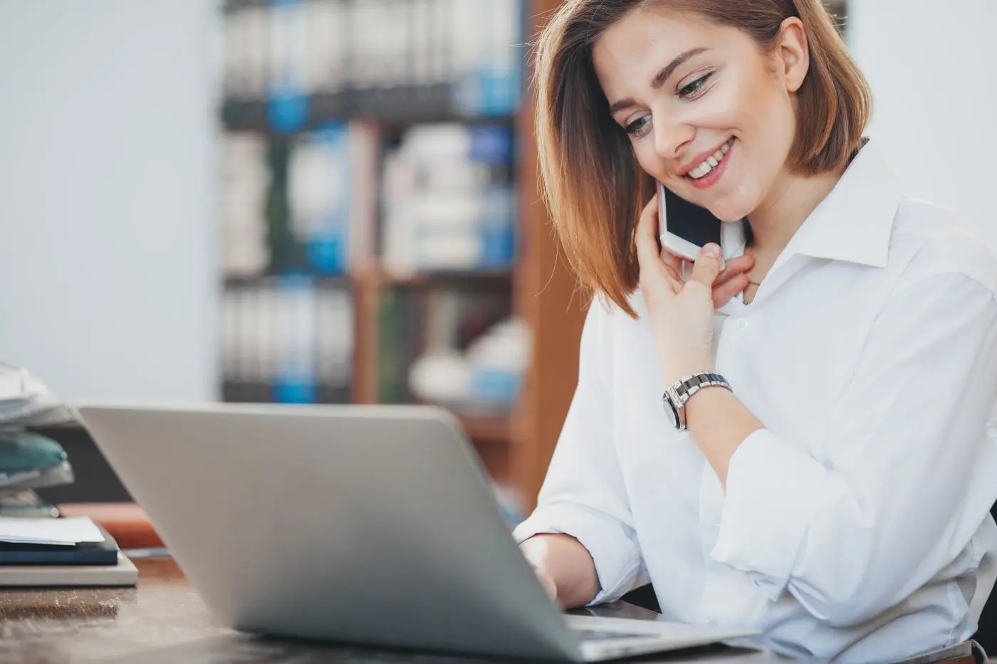 Frau telefoniert und arbeitet gleichzeitig am Laptop.