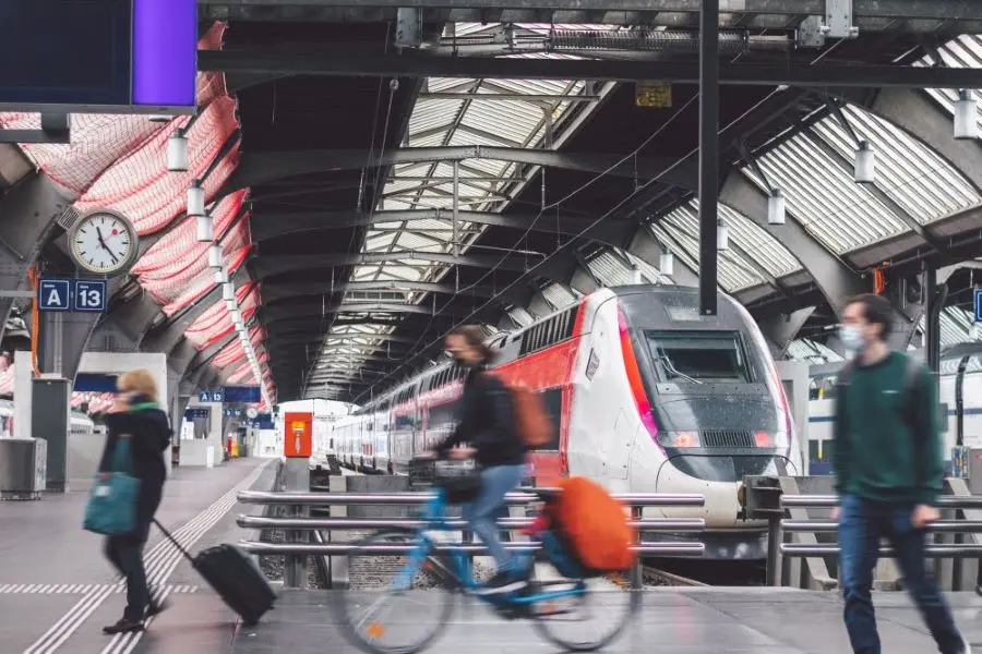 Zug steht in einem Bahnhof, Menschen laufen über den Bahnsteig.