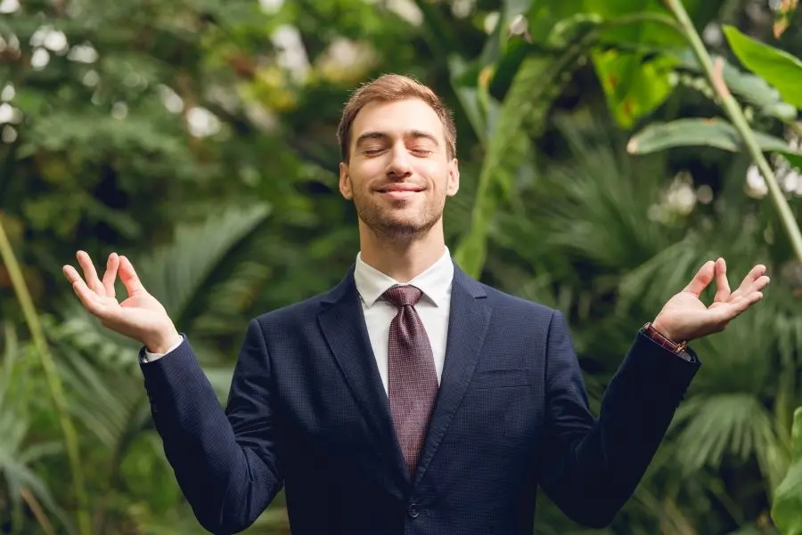 Mann im Anzug steht lächeln und in Meditationspose in einem Dschungel.
