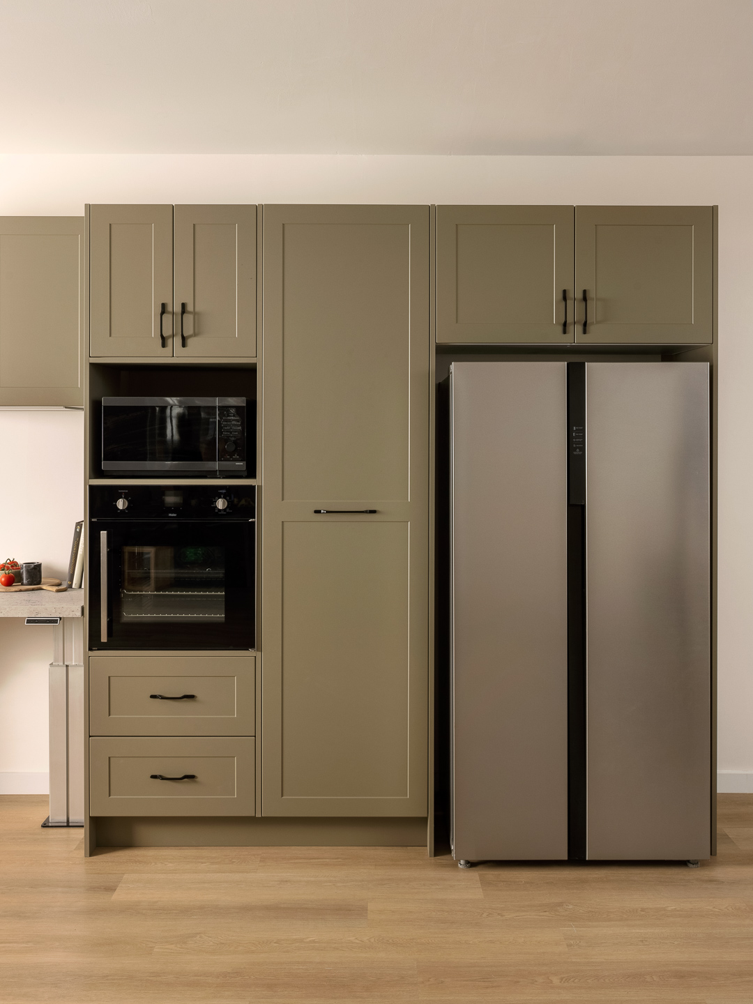 Modern kitchen with olive grove cabinets, built-in oven, and a side-by-side stainless steel refrigerator on wooden flooring.