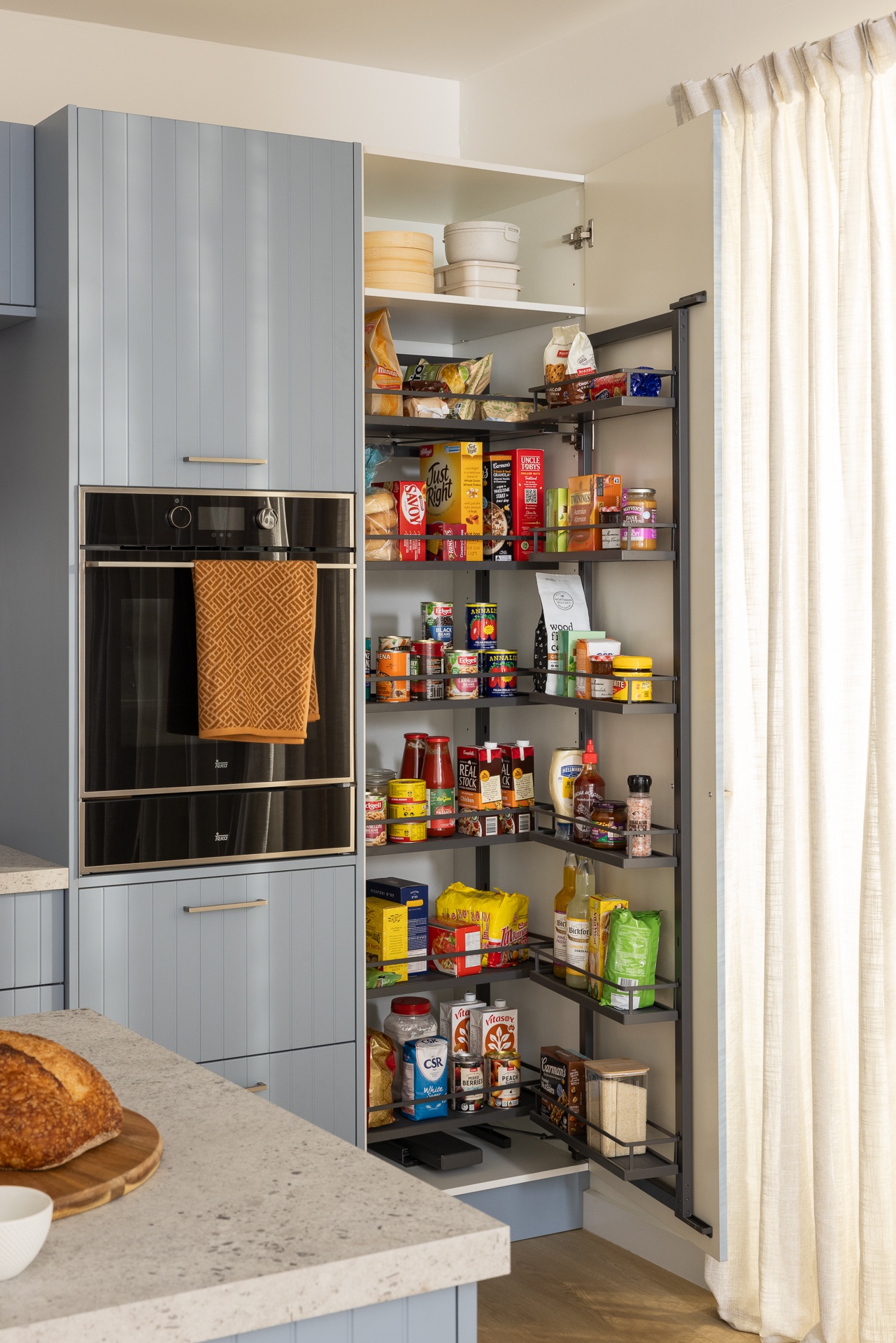 A Pull Out Pantry revealing neatly organised shelves filled with various food items and kitchen supplies.