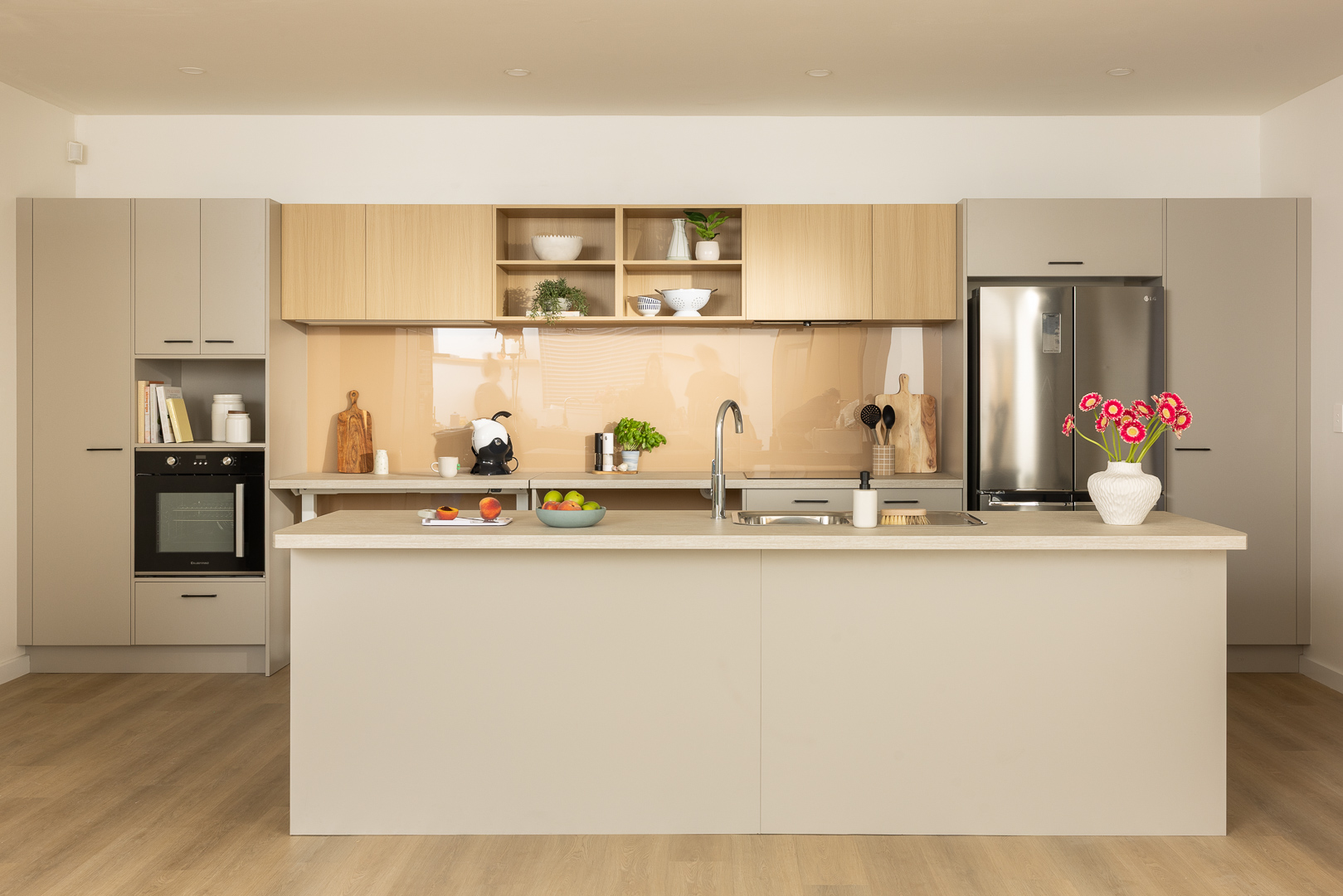 Modern kitchen with light wood cabinets, central island with sink, stainless steel appliances, and decorative items on the countertop.