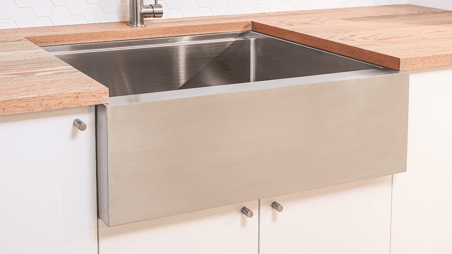 Stainless steel farmhouse sink with wooden benchtops and white cabinetry.