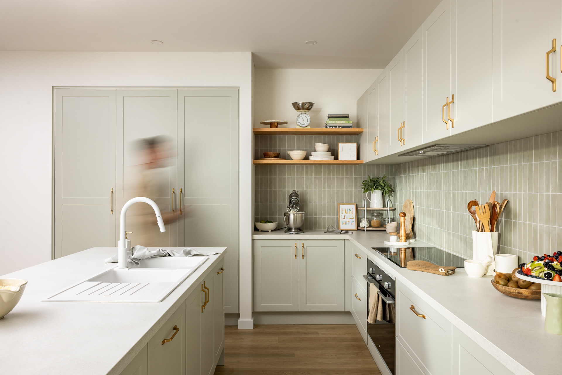 A scandi style kitchen with sage green cabinets, gold accents, and a sleek stone-look benchtop
