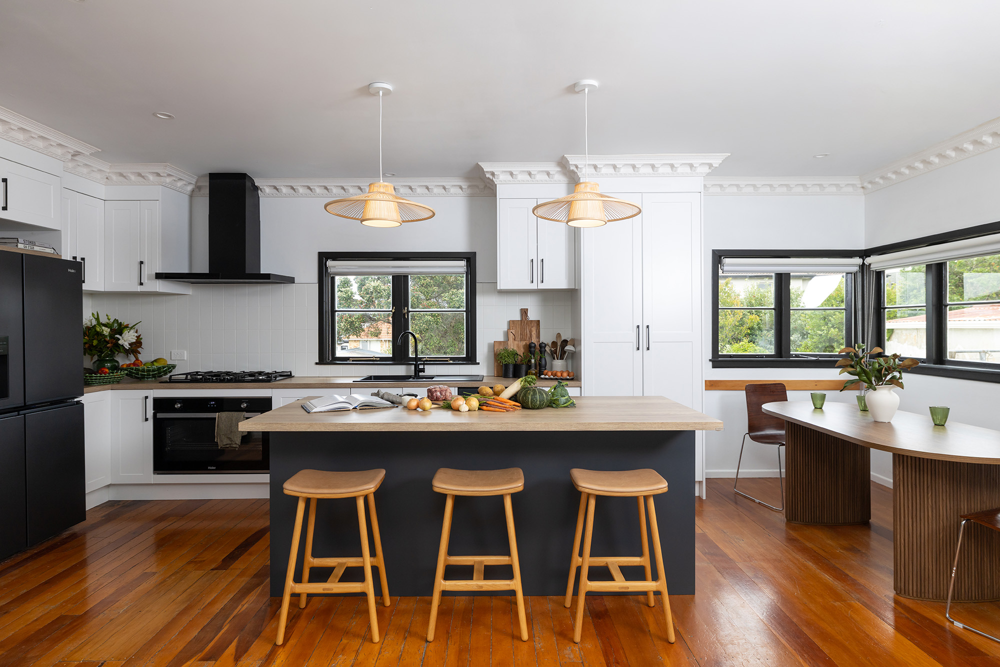 Modern kitchen with white cabinets, black appliances, and a central island with stools. Two pendant lights hang above the island.