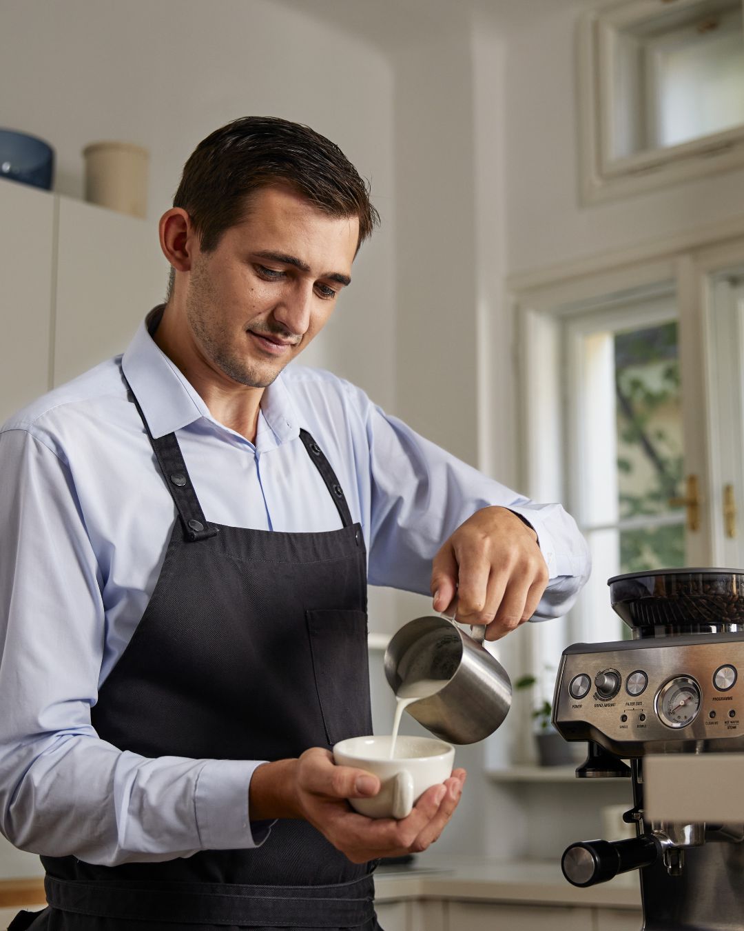 Junger Mann bereitet Kaffee mit Milchschaum vor