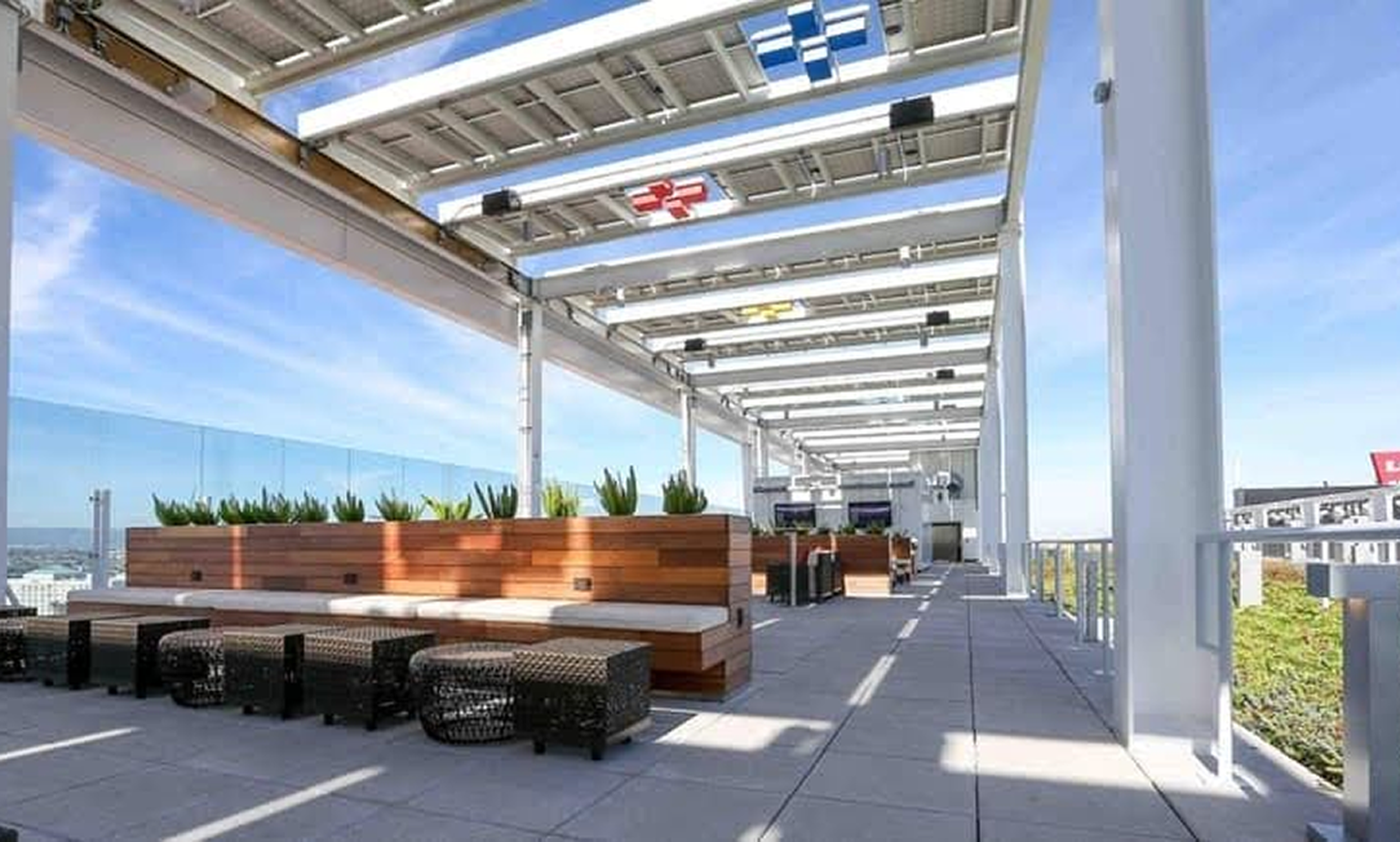 Rooftop terrace with modern seating, potted plants, and an open view of the city, under a grid-patterned canopy on a clear day.