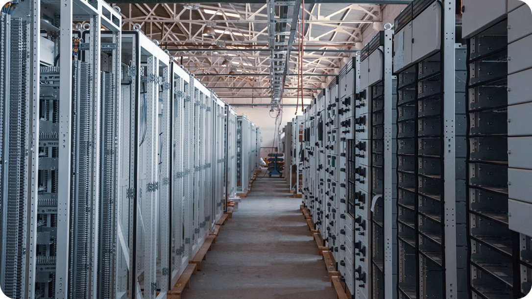 A spacious data center with rows of tall server racks on both sides, creating a symmetrical and organized corridor under a high metal ceiling.