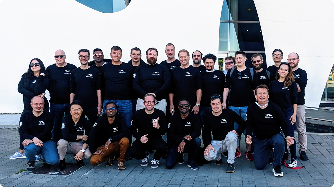 A group of people wearing matching black shirts with a logo, posing together outside a modern building.