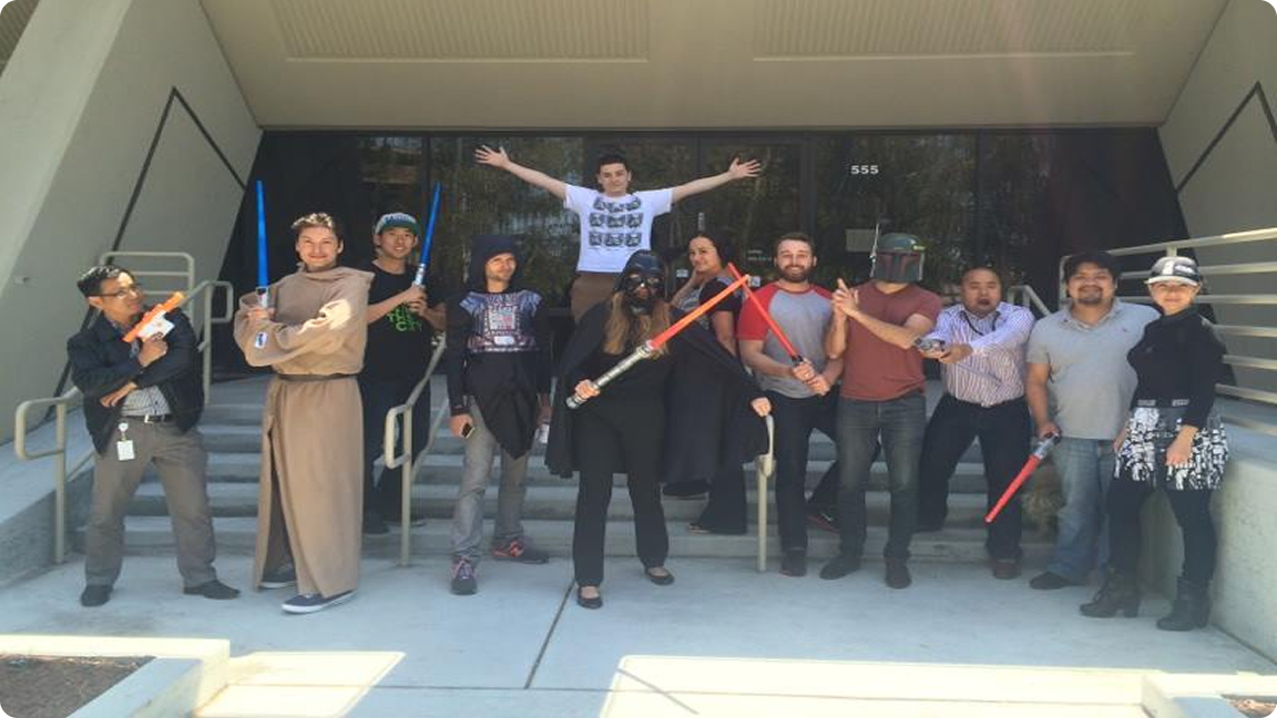 Group of people in Star Wars costumes, holding lightsabers and toy weapons, pose on steps outside a building.