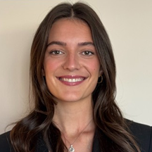 Smiling woman with long brown hair wearing a black blazer, against a plain background.