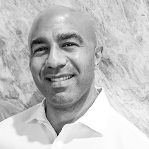 Smiling man in a white shirt against a marble-patterned background, black and white photo.