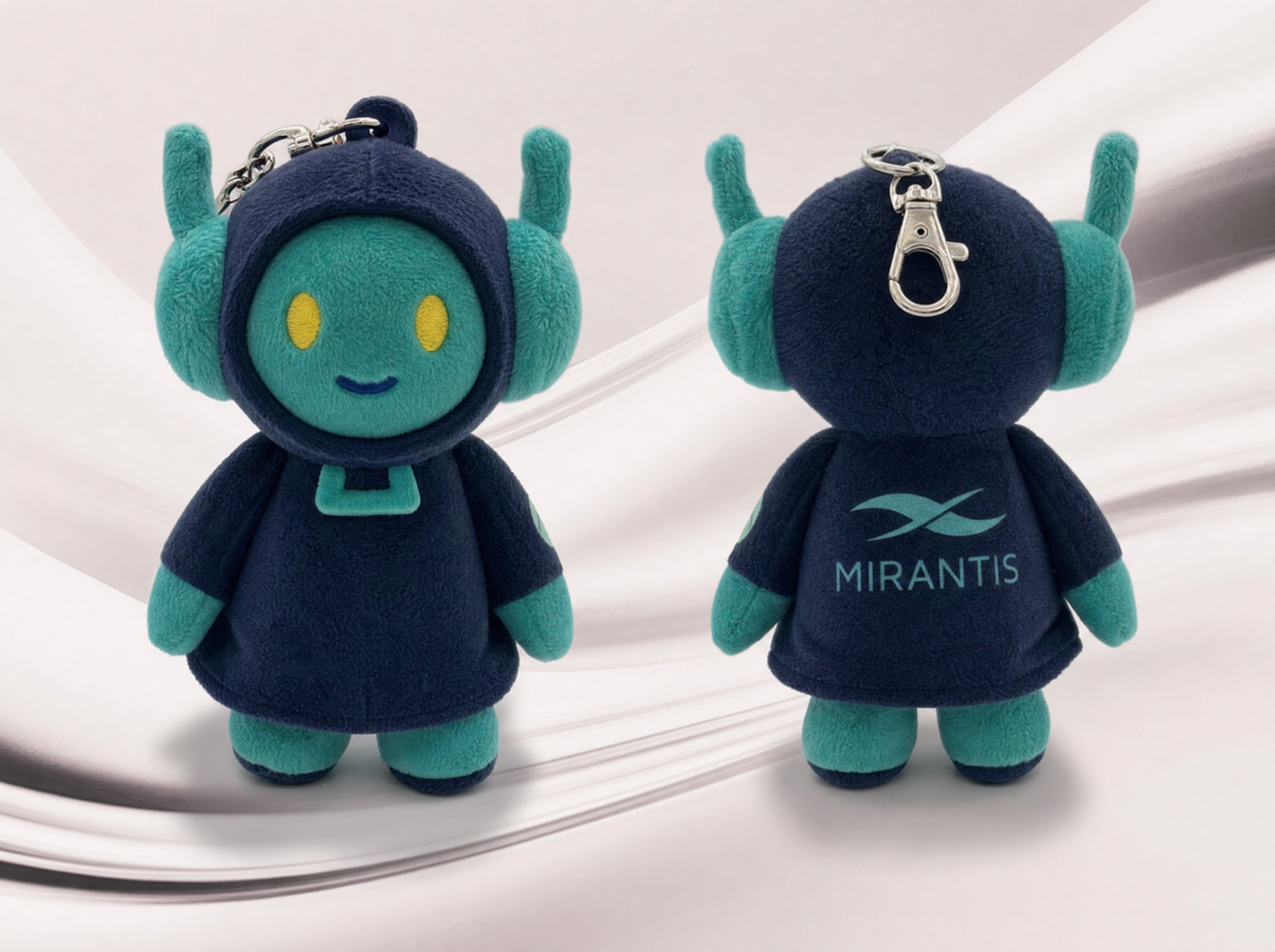 Two small plush robots, teal and navy, with antennae and yellow eyes. One shows a Mirantis logo on the back, each with a keychain clip.