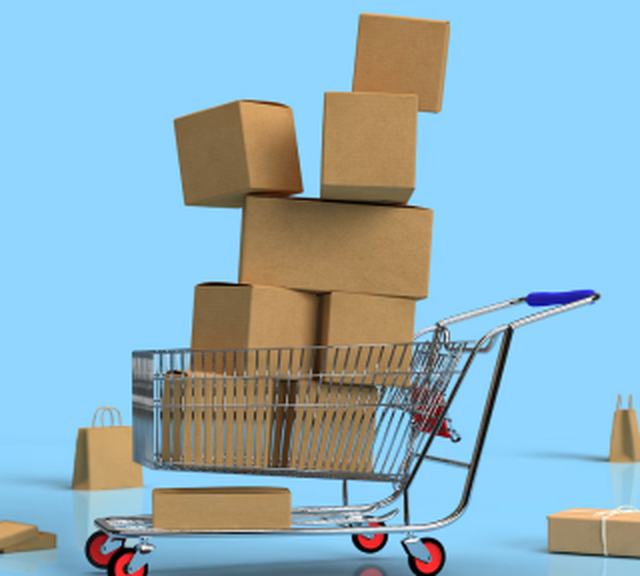 A shopping cart loaded with stacked cardboard boxes against a blue background, with additional bags and boxes nearby.