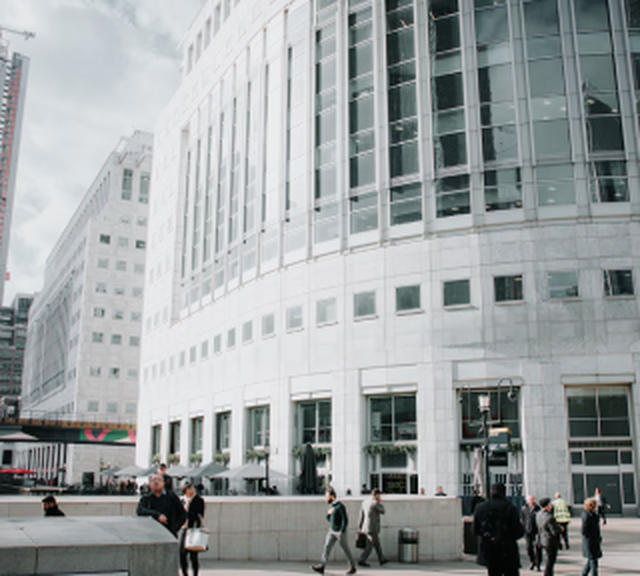 People walking near a large, modern office building with reflective windows on a cloudy day.