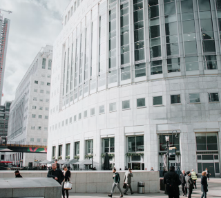 People walking near a large, modern office building with reflective windows on a cloudy day.