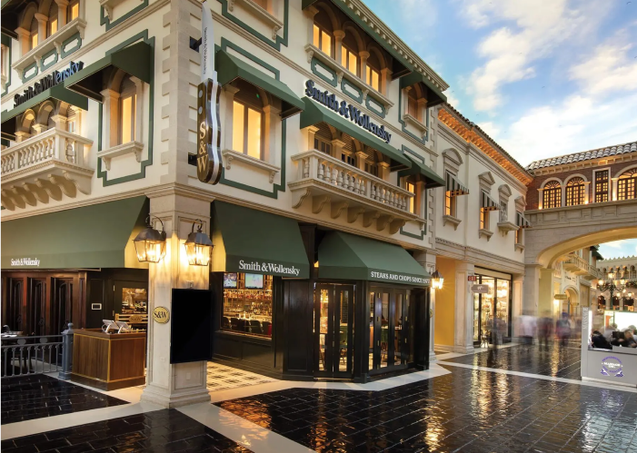 An elegant restaurant exterior with green awnings, warm lighting, and classic architectural details under a blue sky.