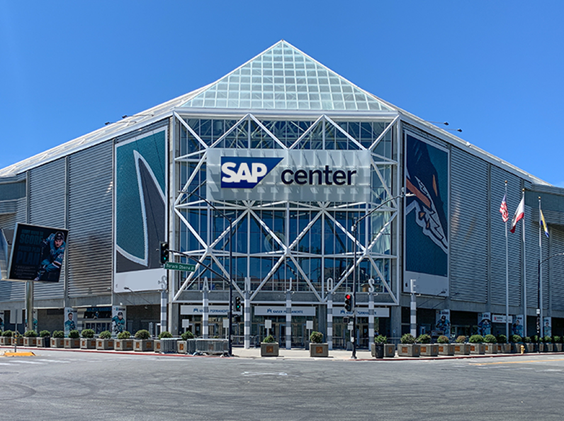 Exterior view of SAP Center, a large glass and steel arena with "SAP Center" signage, featuring geometric design elements under a clear blue sky.