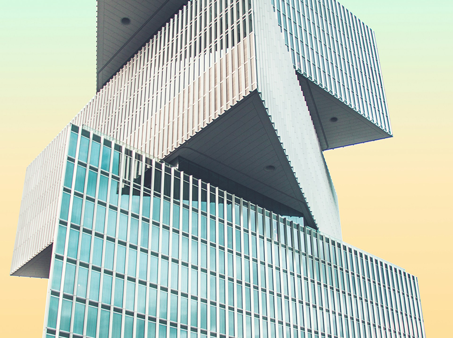A modern building with stacked, offset rectangular sections featuring glass and metal facades against a gradient sky.