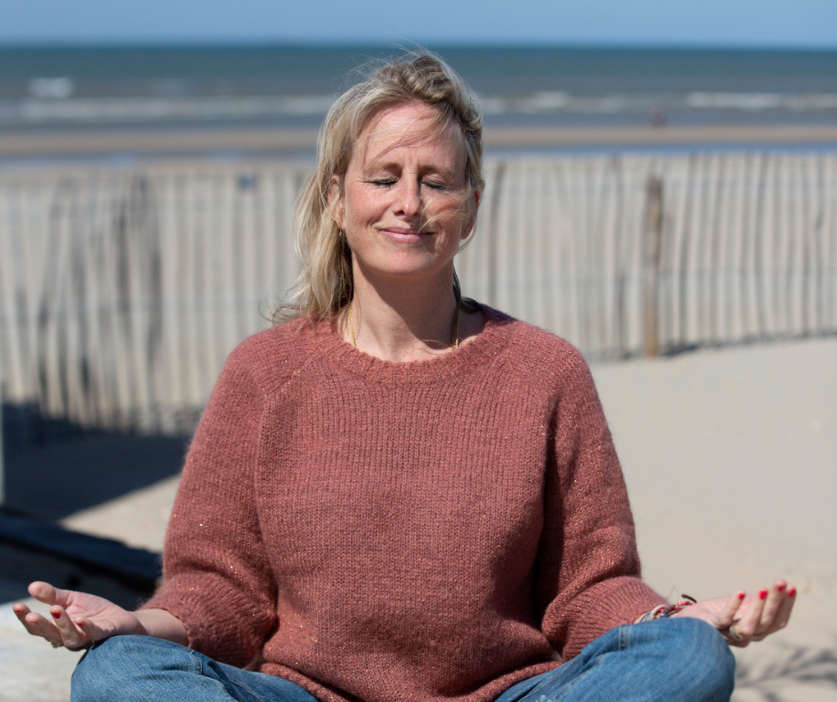 Vrouw op het strand aan het mediteren met haar ogen dicht en benen over elkaar.