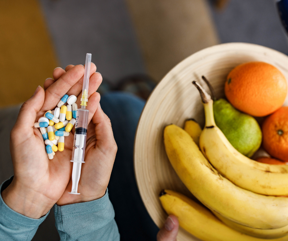 Handen die pillen en een spuit vasthouden naast een mand met fruit.