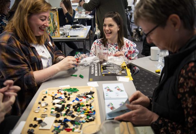 Three people laughing while building Lego at a brick club