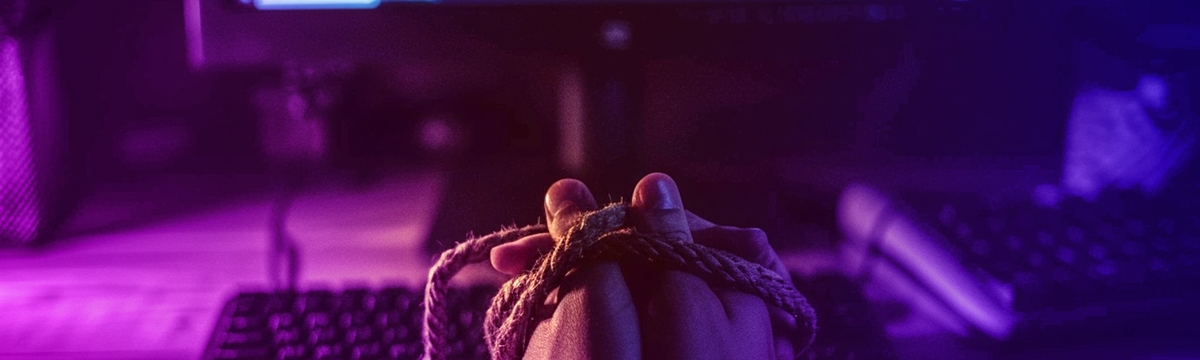 A web developers hands tied together in front of a screen with code on it in a dark room